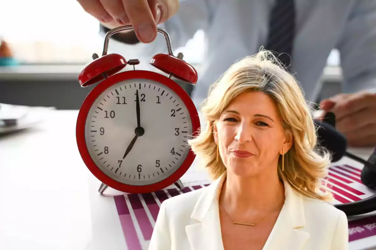 Persona rubia con chaqueta blanca frente a un reloj despertador rojo.