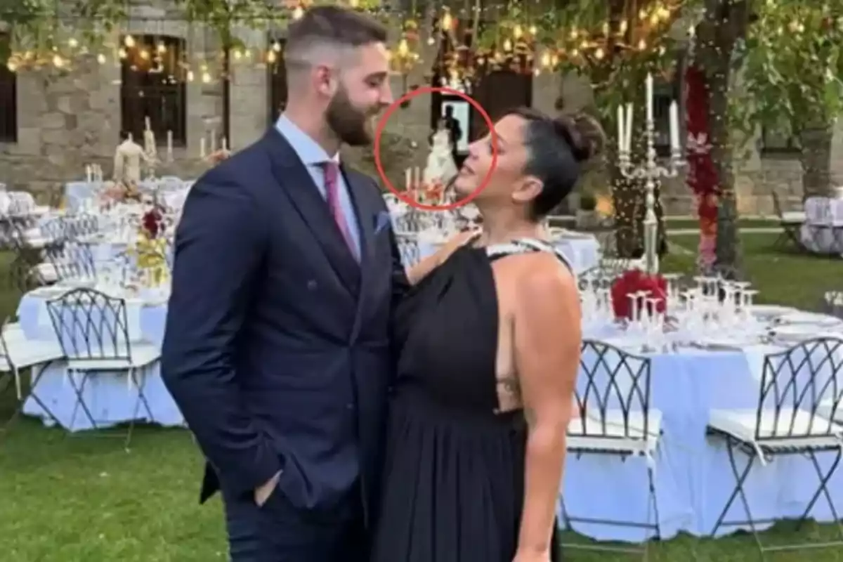 Pareja posando en un jardín decorado para una boda con mesas y luces, mientras al fondo se observa a una novia enmarcada en un círculo rojo Pareja posando en un jardín decorado para una boda con mesas y luces, mientras al fondo se observa a una novia enmarcada en un círculo rojo