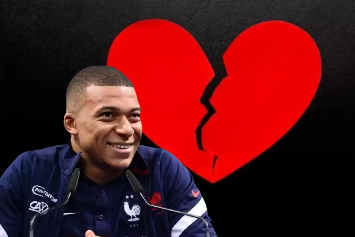 Kylian Mbappé sonriente delante de un fondo con un corazón rojo medio roto