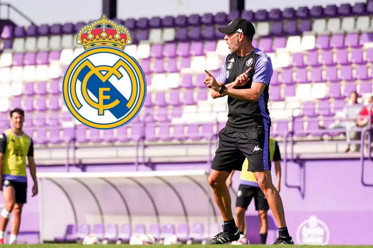 Entrenador de fútbol dando instrucciones en un campo con gradas moradas y el escudo del Real Madrid en primer plano.