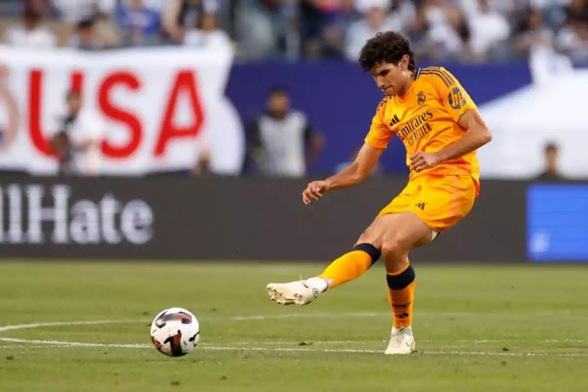 Jugador de fútbol con uniforme naranja pateando un balón en un estadio.