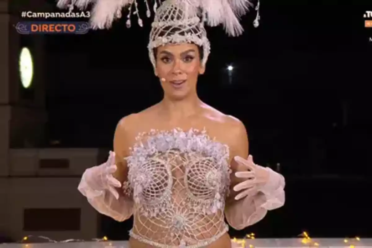 Una persona vestida con un elaborado traje de fantasía con detalles de encaje y plumas en la cabeza, en un evento transmitido en vivo. Una persona vestida con un elaborado traje de fantasía con detalles de encaje y plumas en la cabeza, en un evento transmitido en vivo.