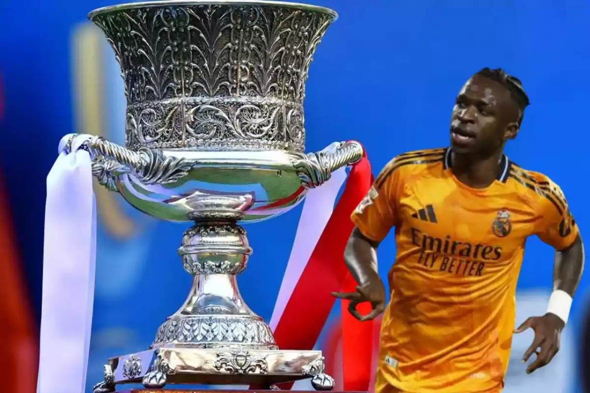 Jugador de fútbol con uniforme naranja junto a un trofeo plateado con cintas blancas y rojas.