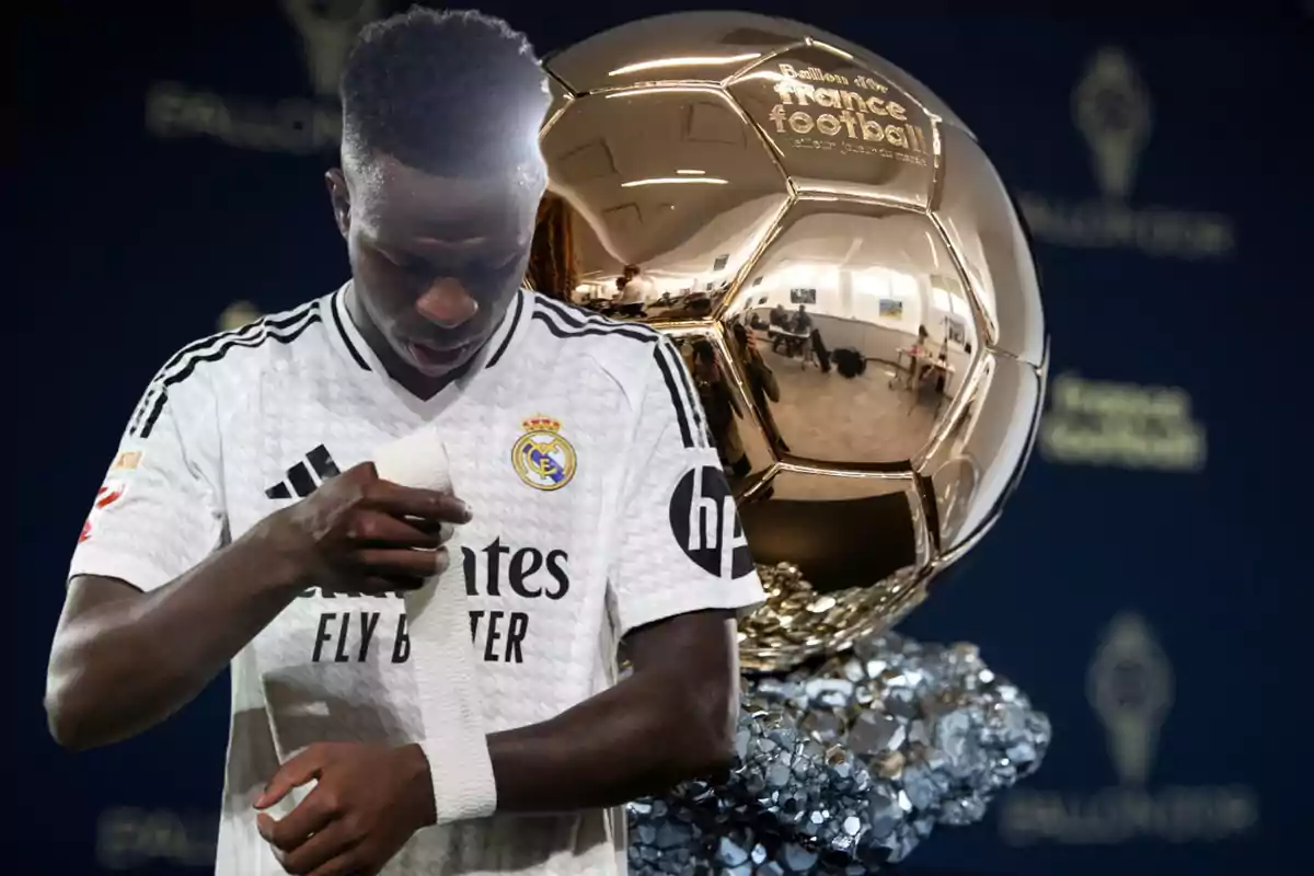 Un jugador de fútbol del Real Madrid ajustándose una venda en la muñeca, con un trofeo del Balón de Oro en el fondo.