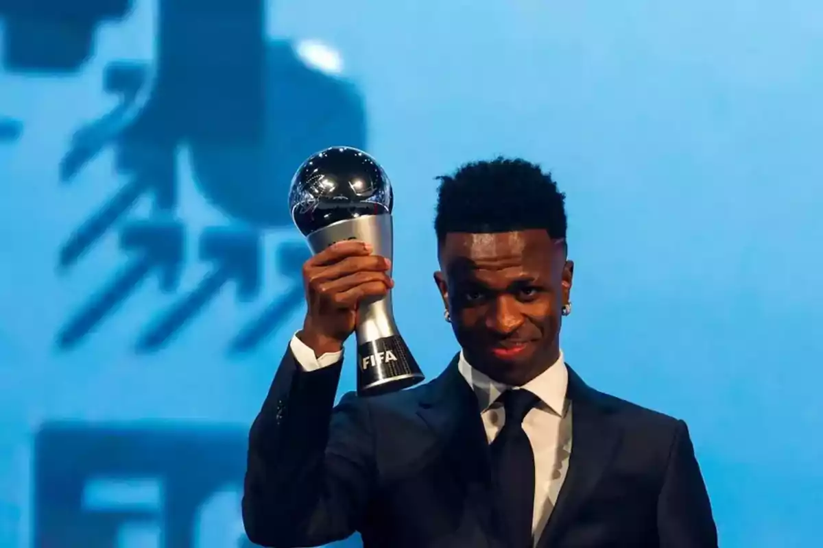 Persona sosteniendo un trofeo de la FIFA en un evento formal. Persona sosteniendo un trofeo de la FIFA en un evento formal.