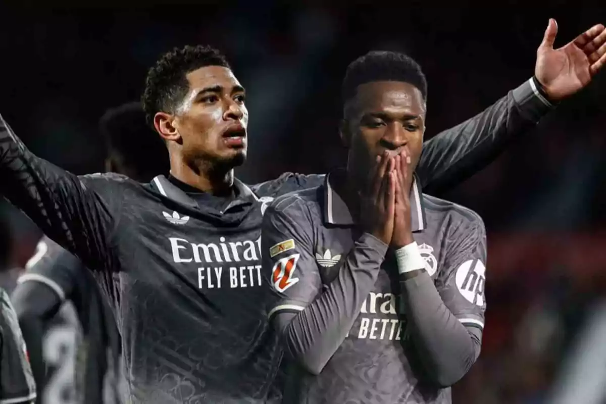 Dos jugadores de fútbol con uniforme gris del Real Madrid en el campo, uno con los brazos levantados y el otro con las manos en el rostro.