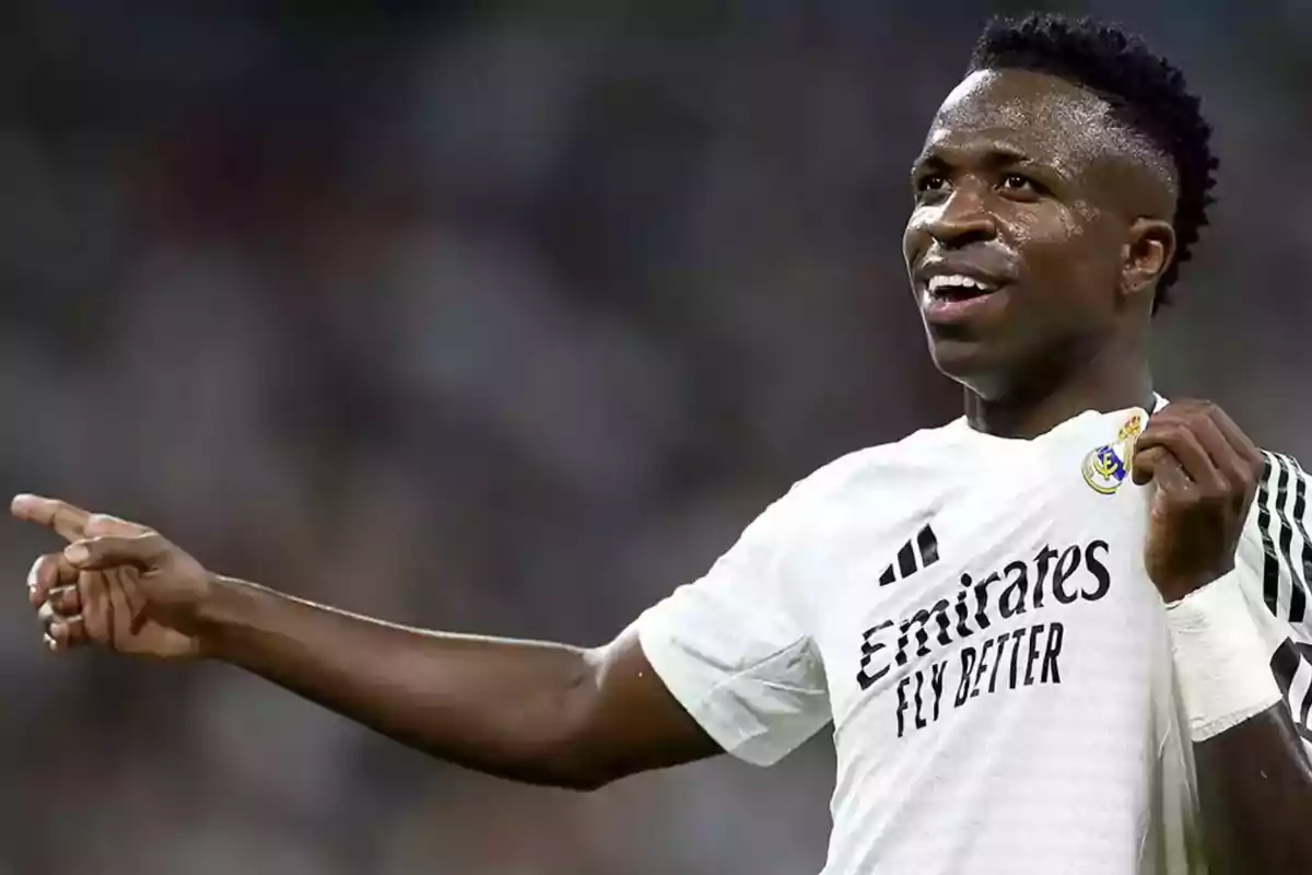 Jugador de fútbol con camiseta blanca señalando hacia un lado en un estadio.