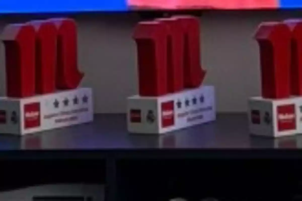 Tres trofeos rojos con forma de "M" sobre una base blanca con estrellas y el logo de Mahou.