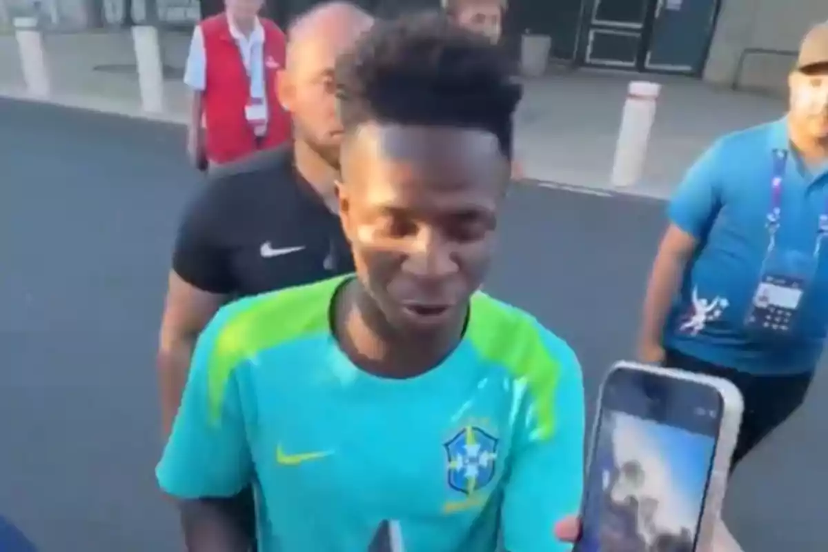 Vinicius Júnior con la camiseta de la selección de Brasil está siendo entrevistado al aire libre, rodeado de varias personas.