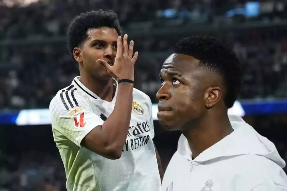 Dos jugadores de fútbol del Real Madrid en el campo, uno de ellos celebrando con un gesto de la mano y el otro mirando hacia arriba.