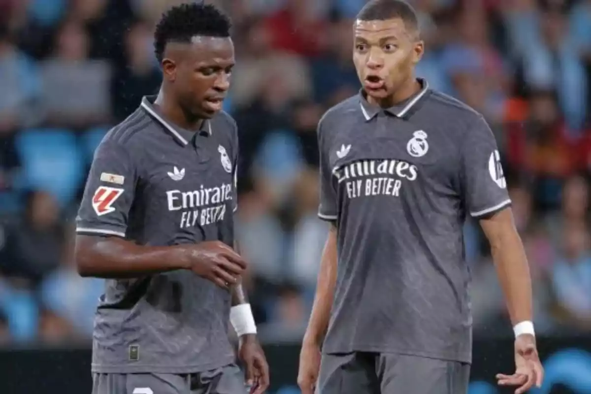 Dos futbolistas en el campo vistiendo uniformes grises del Real Madrid durante un partido.