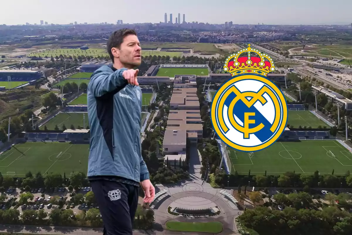 Un hombre con ropa deportiva señala hacia adelante con un complejo deportivo y el escudo del Real Madrid de fondo.