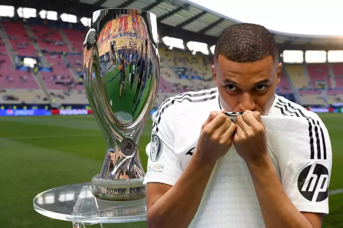 Un jugador de fútbol besa su camiseta junto a un trofeo en un estadio.