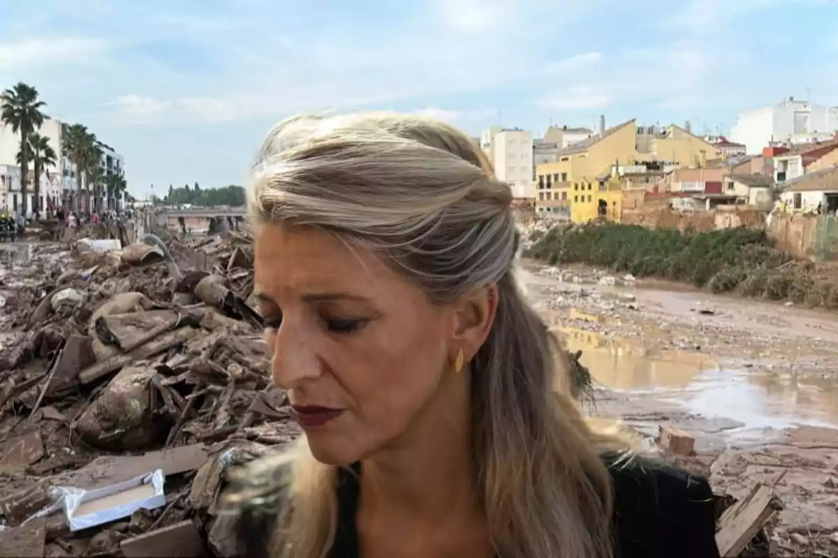 Una mujer de cabello rubio aparece en primer plano con un fondo de escombros y edificios afectados por una inundación.