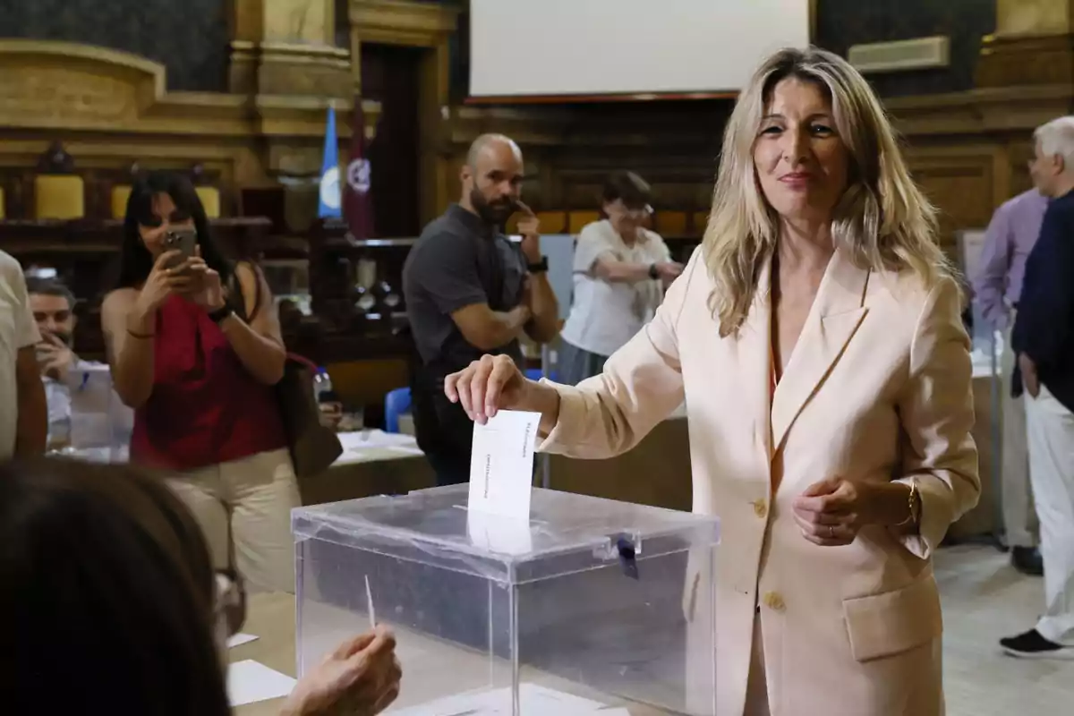 Yolanda Díaz con traje de chaqueta claro depositando el voto en una urna electoral