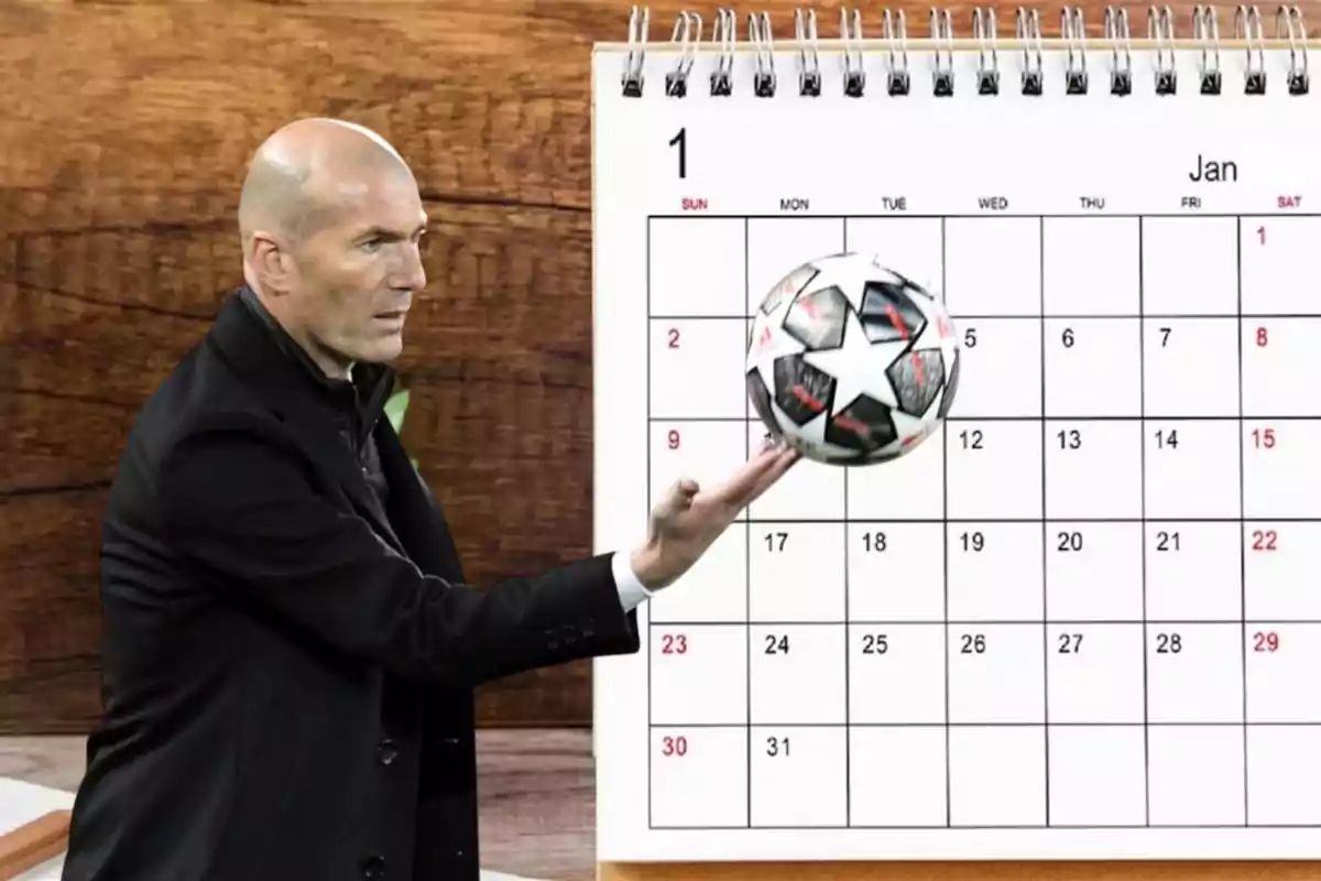 Un hombre calvo con traje oscuro sostiene un balón de fútbol frente a un calendario de enero.